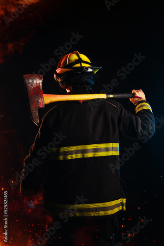 Fireman on his back, holding a hammer, wearing a special protection uniform.  Black background.  Night and fire.