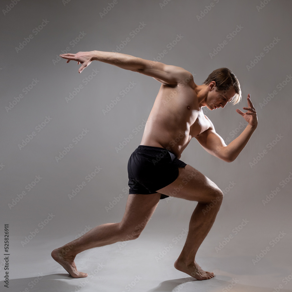 A young muscular man in an expressive pose, as an ancient Spartan hero. Beautiful muscles. extraordinary athletic body. Portrait on a gray background