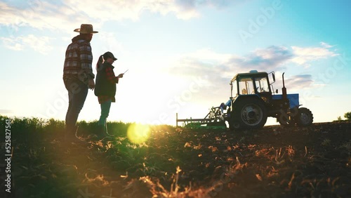 Silhouette farmer woman and man engineer with digital tablet walking in field in rays of sunset on field. Teamwork in agribusiness. Farmers inspect their rural surroundings. Summer walk in nature. photo