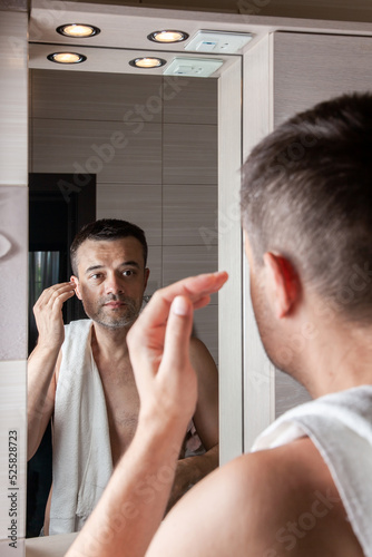 A man looks in the mirror in the morning and straightens his hair in the bathroom with a towel on his shoulder