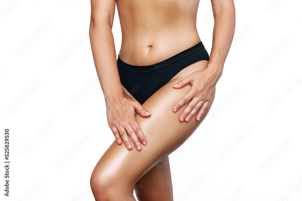 Cropped shot of young slender tanned woman smearing her thigh  with cosmetic oil isolated on a white background. Cosmetology, massage, spa products. Skin care