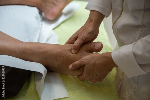 Um profissional fazendo massagem terapêutica no pé do paciente que está deitado na maca.