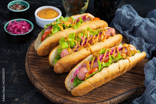 Hot dog with lettuce, tomatoes and pickled onions. Grilled bun with sausage
