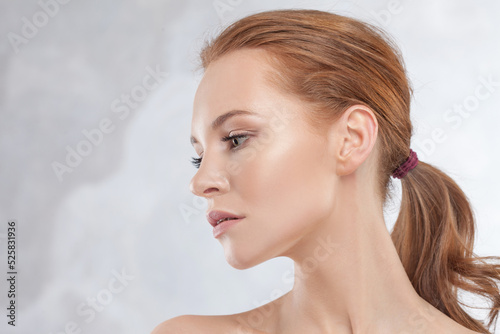 A young attractive red-haired woman with clear skin, portrait in profile on a light gray background. Beauty and facial care