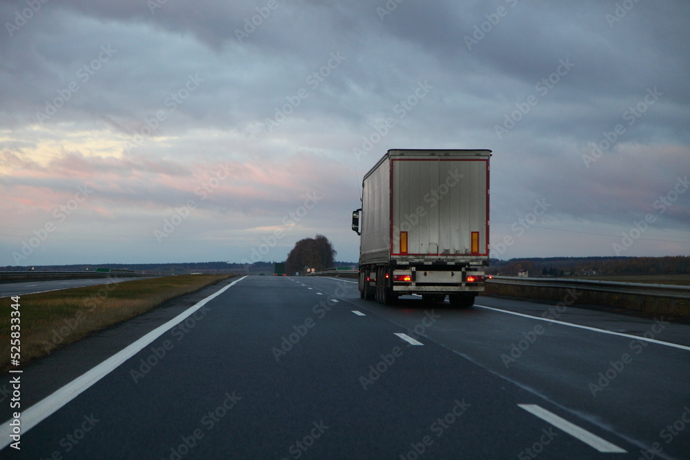 White heavy truck on countryside highway road on dramatic clouds background. Uhfnsportation logistics in Europe