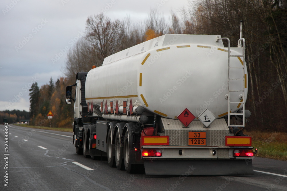 Modern semi truck fuel tanker with 33-1203 dangerous class sign move on suburban highway road at autumn evening in perspective, back view, gasoline fuel ADR cargo transportation logistics in Europe