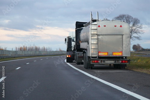 Gray fuel tanker truck on roadside on heavy clouds baqckground. Hazardous goods cargo logistics in Europe