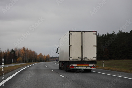 Obraz na płótnie Heavy white semi truck back view on two-lane countryside asphalted road at autumn evening on gray cloudy sky background w salonie