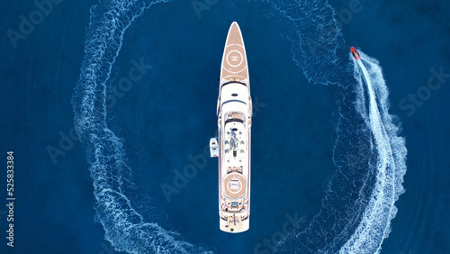 Aerial drone top down photo of stunt man performing extreme stunts and circling with jet ski watercraft over anchored yacht in deep blue ocean sea