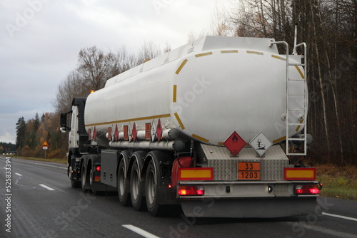 Obraz na płótnie Petrol transportation, white fuel tanker truck with ADR sign 33 1203 on suburban empty asphalted road at autumn evening on forest background, flammable liquid goods transportation w salonie