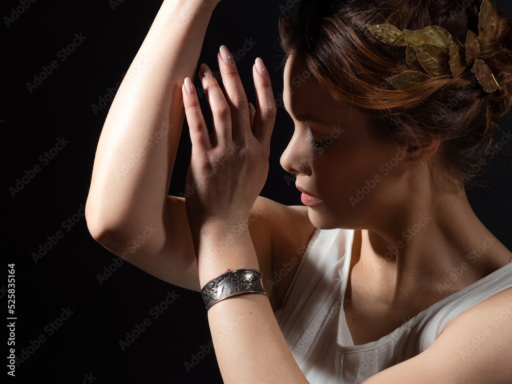 A beautiful ancient goddess from the era of the heroes of Hellas. A young woman in a white tunic and a laurel wreath, an ancient Greek muse or heroine, close-up on a contrasting black background