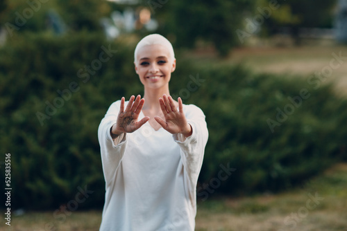 Fototapeta Naklejka Na Ścianę i Meble -  Portrait of young smiling millenial european short haired woman doing Qigong in summer park. Beautiful happy blonde girl outdoor.