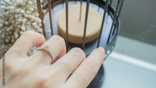 Close up of an elegant diamond ring on woman finger while touching white flower with sunlight and shadow background. love and wedding concept. Soft and selective focus.