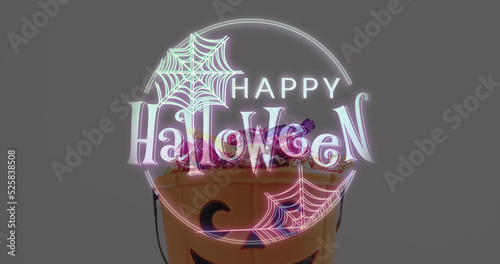 Halloween text banner with spider web icon against pumpkin shaped bucket full of halloween candies