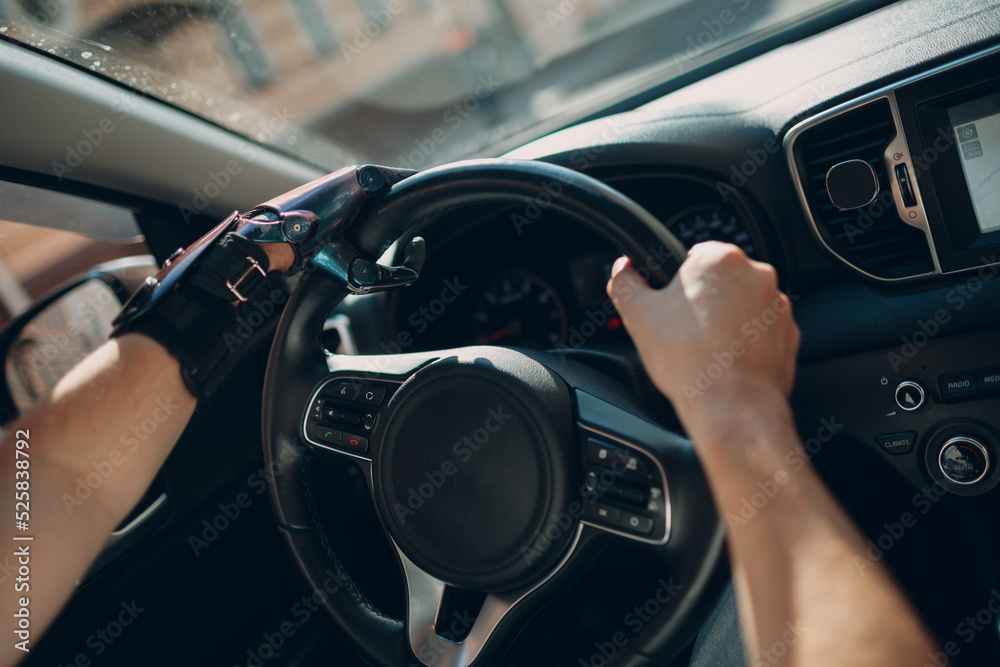 Obraz premium Young disabled man driver with artificial prosthetic hand driving on steering wheel vehicle car