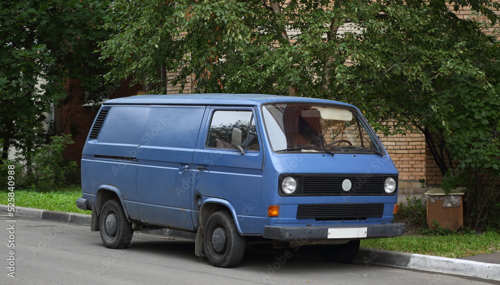 An old blue minibus is parked near the lawn, Kollontai Street, St. Petersburg, Russia, August 2022