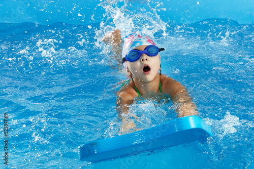 Obraz na płótnie Little girl learning to swim in indoor pool with pool board