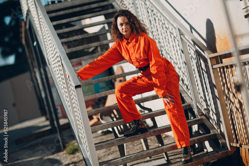 Young brunette curly woman in orange suit. Female in colorful overalls portrait