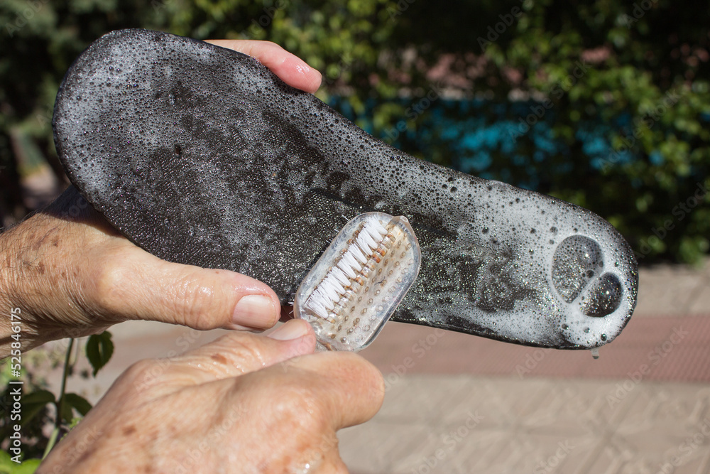 Hands brushing a shoe insole with soap and bubbles outside in broad