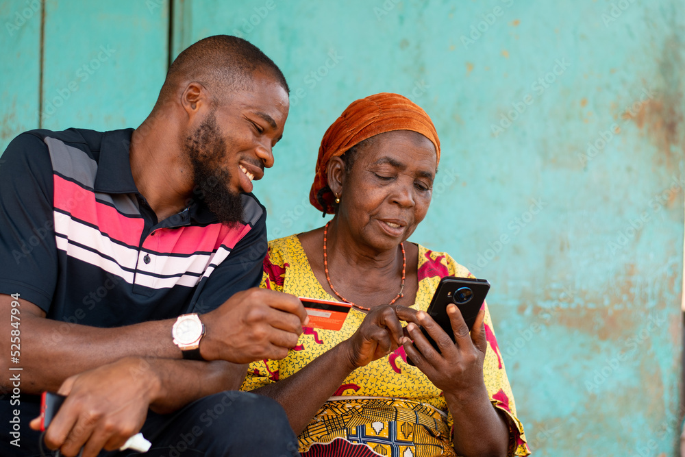 elderly african woman and young man use phone and credit card - obrazy, fototapety, plakaty 