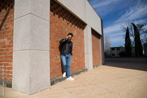 middle-aged man, handsome and dark, bearded and with a sculpted body on a brick wall. Man wearing black leather jacket, mirrored sunglasses, and jeans. Man poses for photo. Men's fashion concept.