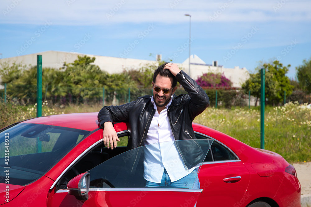 Handsome young man, sculpted body next to his red sports car. The man is wealthy and dressed in modern clothes. Sports car