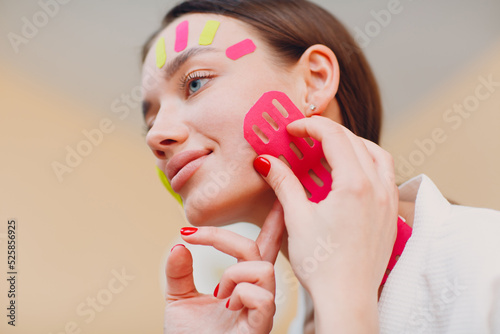 Beautiful woman applying tape lifting treatment procedure on face