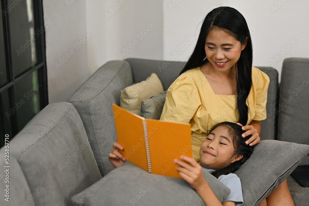Daughter laying down on Mom's lap during reading a book together, Happy family are spending time together, Mother's day concept. Daughter laying down on Mom's lap during reading a book together, Happy family are spending time together, Mother's day concept.