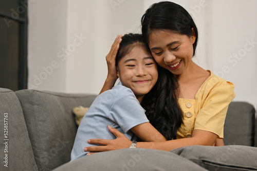 Affectionate loving middle aged mother cuddling grownup child, Excited to see daughter, happy mom cuddling her daughter, sitting together on comfortable sofa in living room.