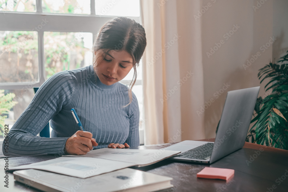 One young pretty woman studying and doing homework at home on the table. Female teenager using laptop or computer surfing the net indoor. One young pretty woman studying and doing homework at home on the table. Female teenager using laptop or computer surfing the net indoor.