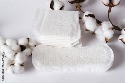 Women's sanitary napkins for the menstrual period unpacked and in a package with natural cotton on a light background