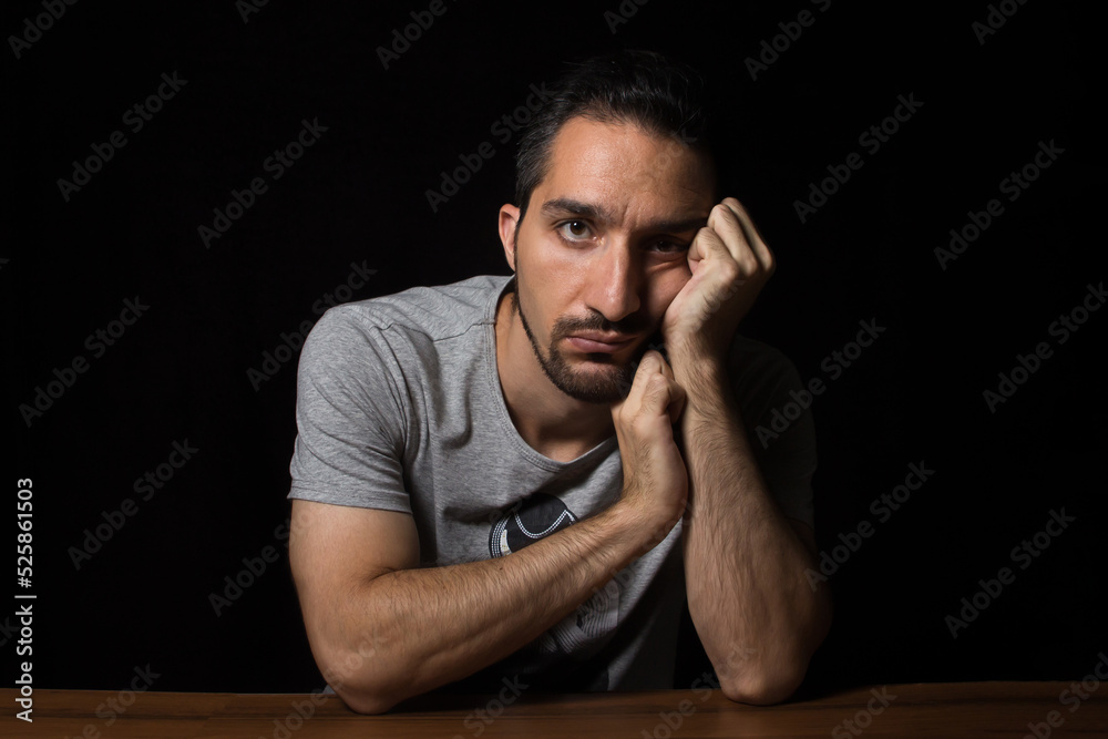 A man with a boring face sits at a table. Male portrait on a black background. A man with a boring face sits at a table. Male portrait on a black background.