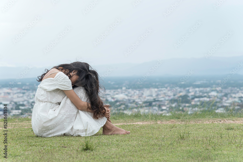 woman sit facing side face down knee on grass at top mountian sky ,city and nature view background. feel sad and depress..