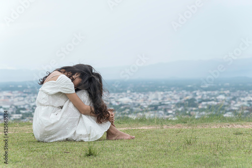Obraz na płótnie woman sit facing side face down knee on grass at top mountian sky ,city and nature view background. feel sad and depress.. w salonie