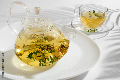 Yellow herbal tea with thyme in glass teapot. White background with copyspace.