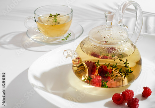 Yellow herbal tea with thyme in glass teapot. White background with copyspace.