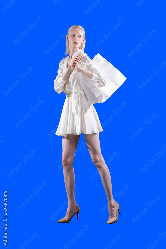 White caucasian albino blond woman holds shopping bag on isolated blue background. Sale and discounts on market and Black Friday concept. White caucasian albino blond woman holds shopping bag on isolated blue background. Sale and discounts on market and Black Friday concept.