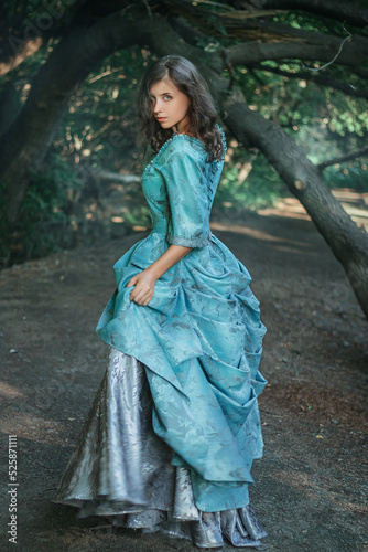 A young woman in a 19th century dress runs away along a forest path, a mystical atmosphere. Historical costume. Woman in a park or forest.