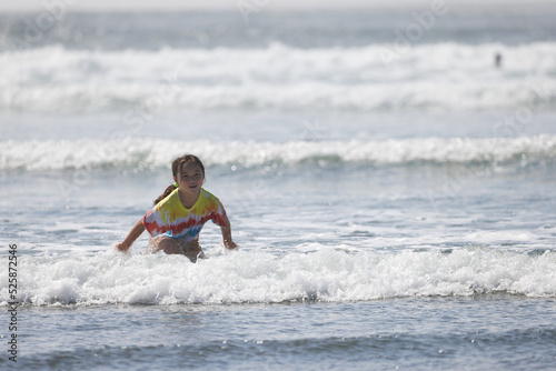 A young girl wearing a tie-dye shirt playing in the water near shore at Westport, Washington. © Derrick