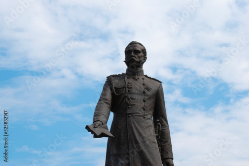 Monument to the Russian Tsar Liberator Emperor Alexander II the second in black against a beautiful light blue sky with clouds in close-up, holding a book or paper. Culture and History of Russia. 