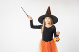 Kids Halloween. A beautiful cute girl in a witch costume, wearing a hat, holding Jack's lantern, with a magic wand shows an empty space on a white background, copy space. The little sorceress.