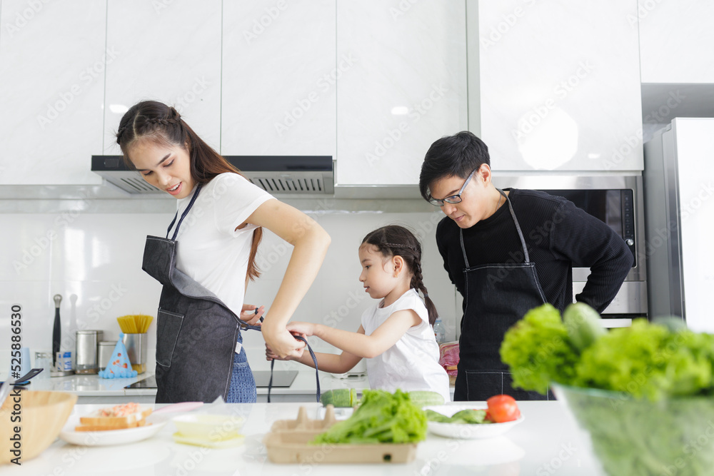 Asian family couple, husband and child help his to put on apron before cooking in the kitchen at home, happy father and son concept. Asian family couple, husband and child help his to put on apron before cooking in the kitchen at home, happy father and son concept.