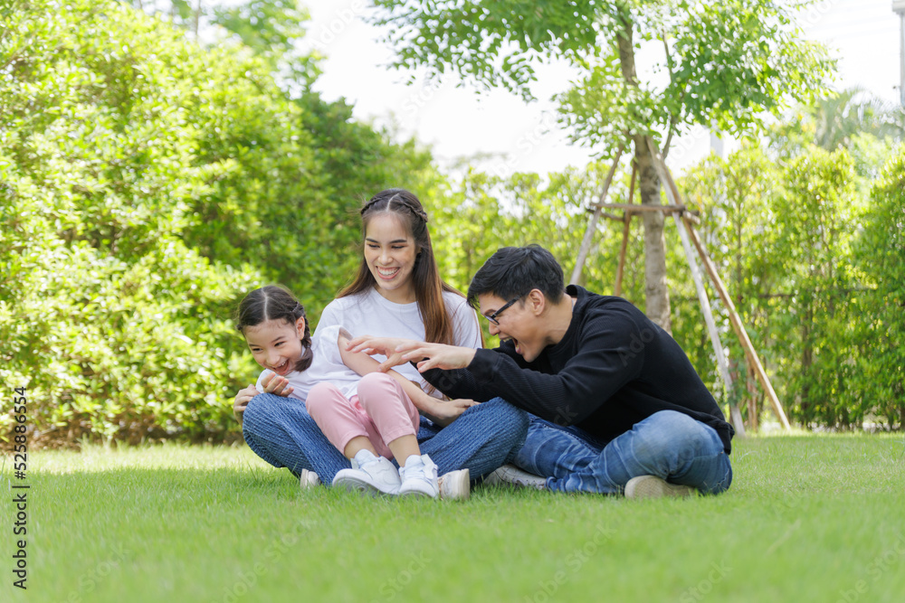 Asian Family with a child playing on a lawn, Family sitting on the grass with her happy and adorable little daughter, enjoyment relaxing recreational concept. Asian Family with a child playing on a lawn, Family sitting on the grass with her happy and adorable little daughter, enjoyment relaxing recreational concept.