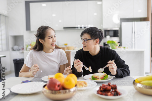 Asian Couple Having Breakfast Sitting In Kitchen