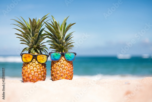 Pineapples in stylish sunglasses on the sand against sea