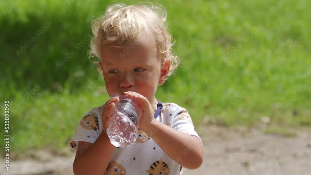 Little child drinking water from a baby bottle in the park in summer, 1.5 year old toddler kid on the nature outdoors. Little child drinking water from a baby bottle in the park in summer, 1.5 year old toddler kid on the nature outdoors.