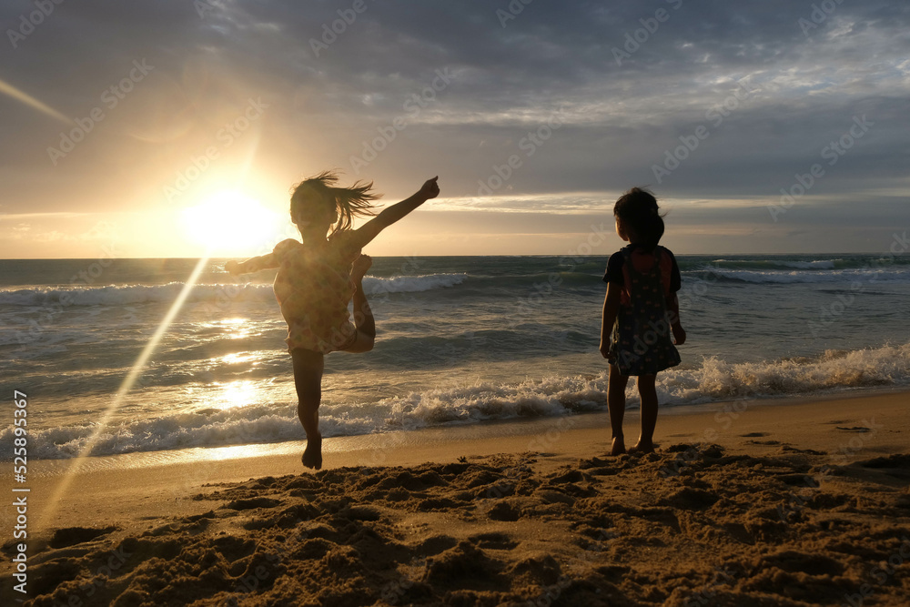 Fototapeta premium Cute Asian sisters playing on the beach during summer vacation at sunset together. Summer family trip to the beach. travel and vacation concept.