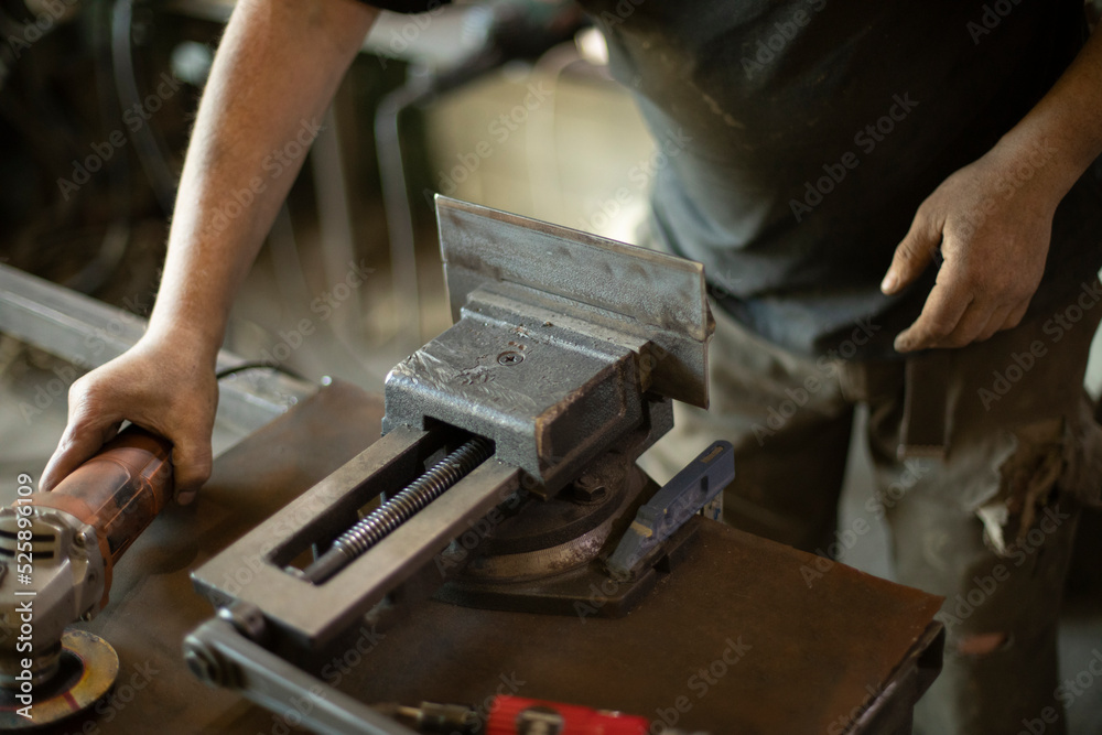 Guy in garage is repairing steel part. Man grinds iron.