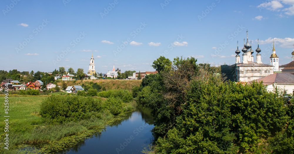 Panoramic top view of the city of Suzdal in Russia with historical architecture and a church among the lush green foliage of trees and a small river on a sunny summer day