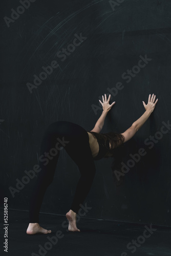 Fototapeta Naklejka Na Ścianę i Meble -  Young woman meditates, doing yoga poses and asana. Fitness girl enjoying yoga indoors. A yoga gymnast girl on a dark background. Black on Black.